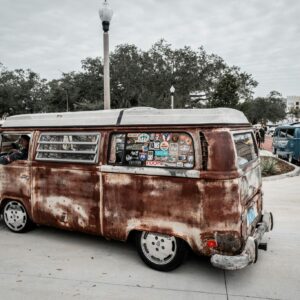 A classic rusted Volkswagen van adorned with stickers at an outdoor car show, evoking nostalgia.