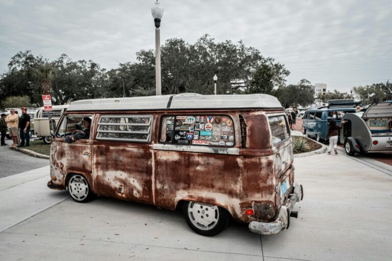 A classic rusted Volkswagen van adorned with stickers at an outdoor car show, evoking nostalgia.