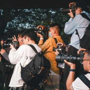 A group of photographers gather outdoors, capturing scenes with their cameras.
