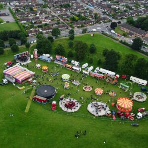 A lively aerial view of an amusement park festival in Luton, England, showcasing rides and green surroundings.
