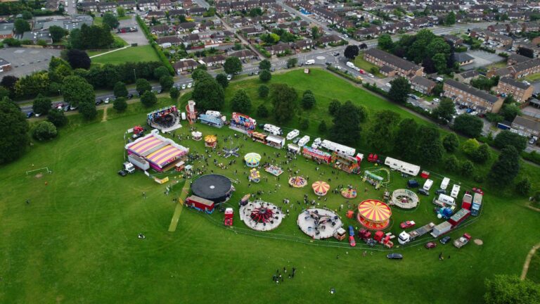 A lively aerial view of an amusement park festival in Luton, England, showcasing rides and green surroundings.