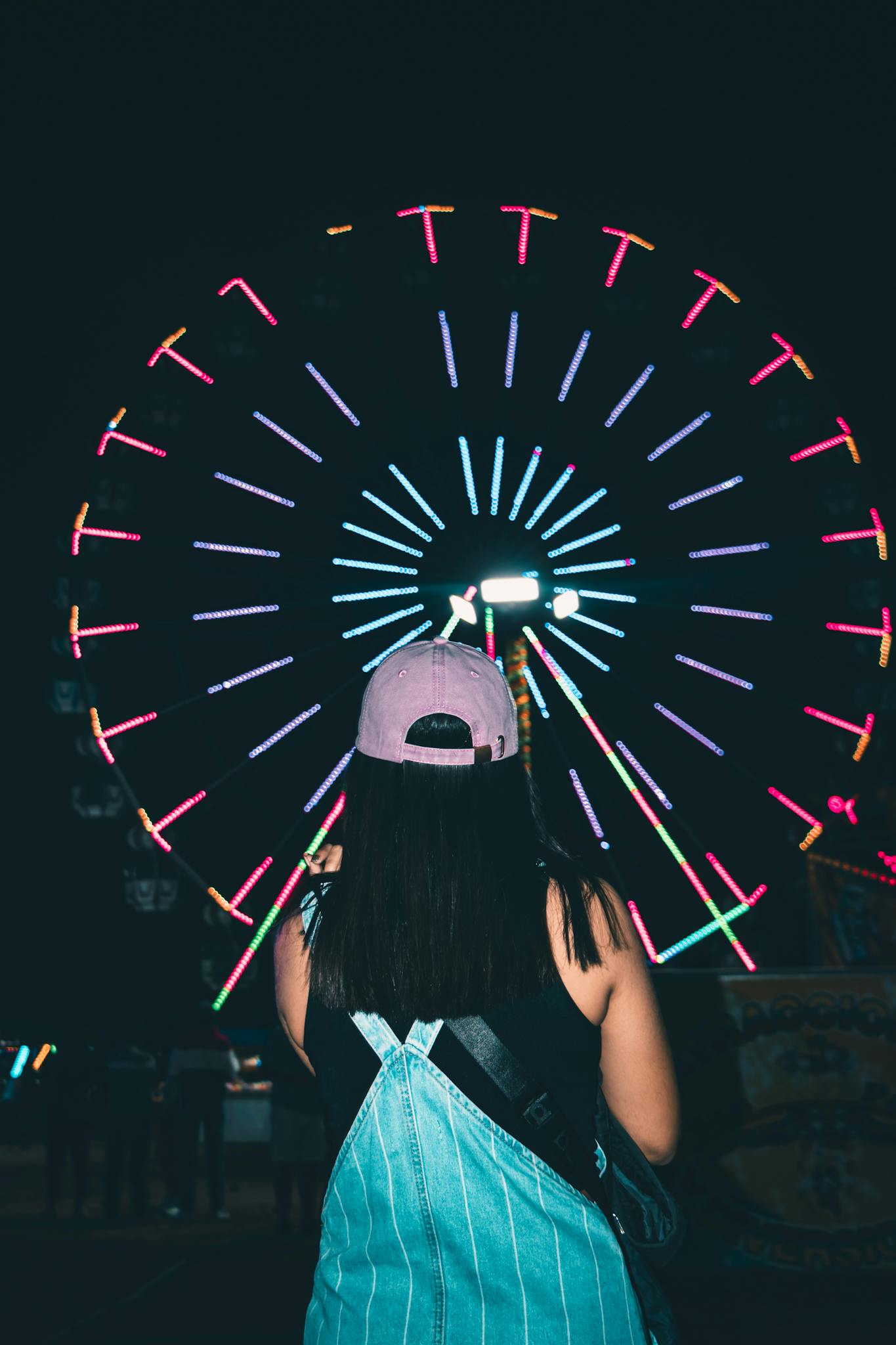 A person gazes at a brightly lit Ferris wheel in Tumbes, Peru, during the night.