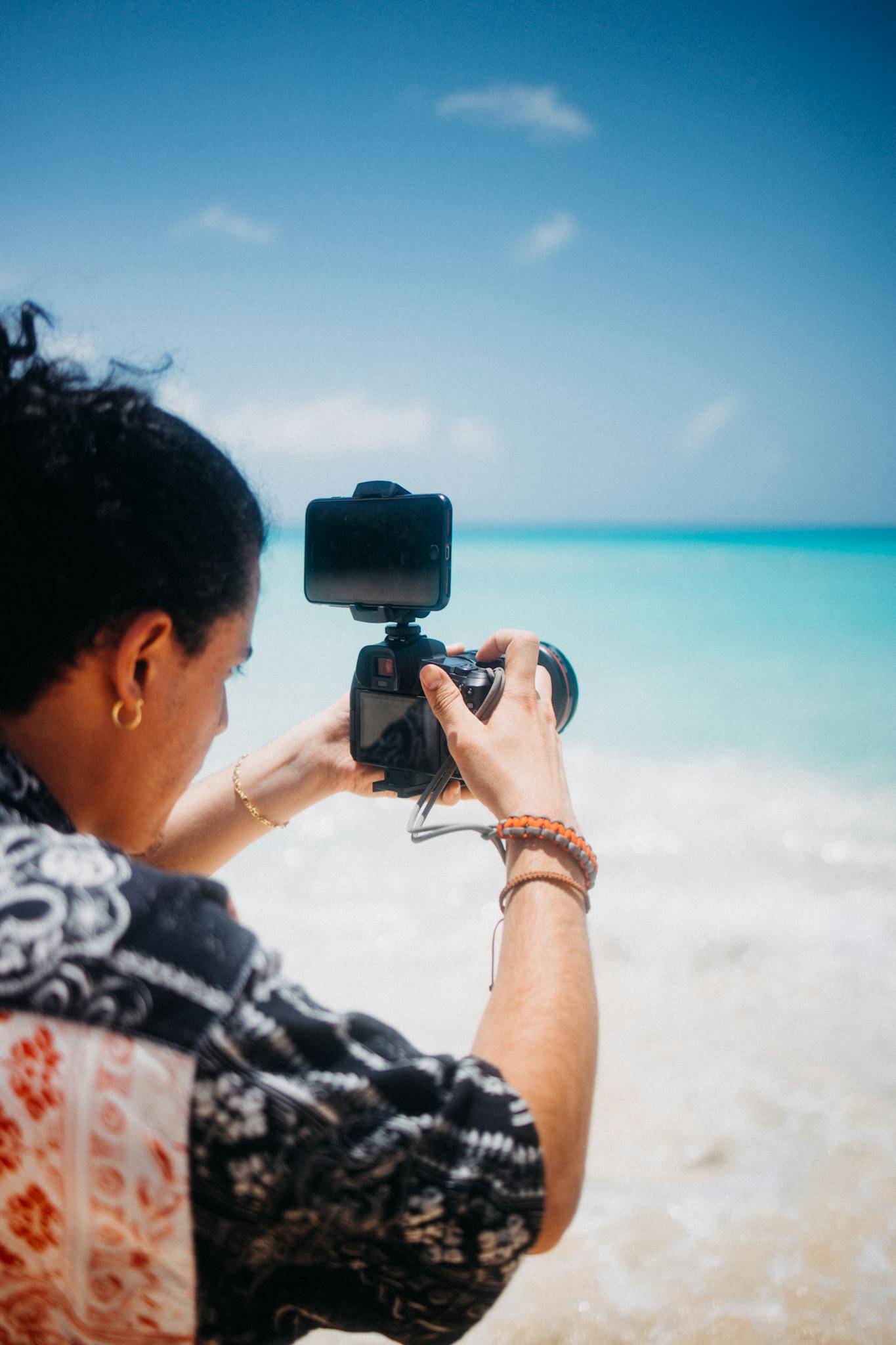 A photographer focuses on capturing a beautiful ocean scene with clear blue waters and a sandy beach.