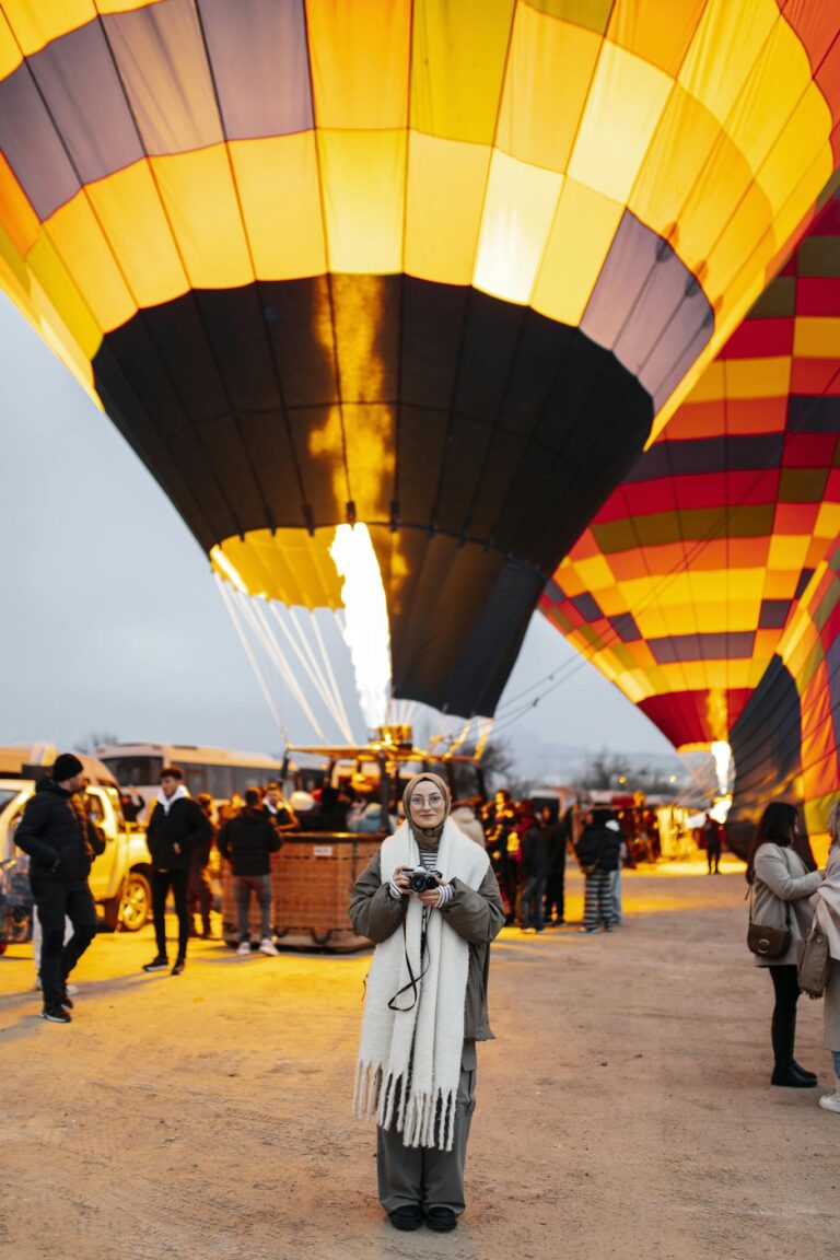 A scenic view of hot air balloons being prepared for flight at dawn with a woman in the foreground.