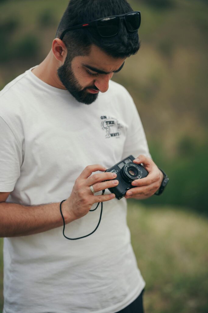 A young man examines a camera outdoors, highlighting photography passion.