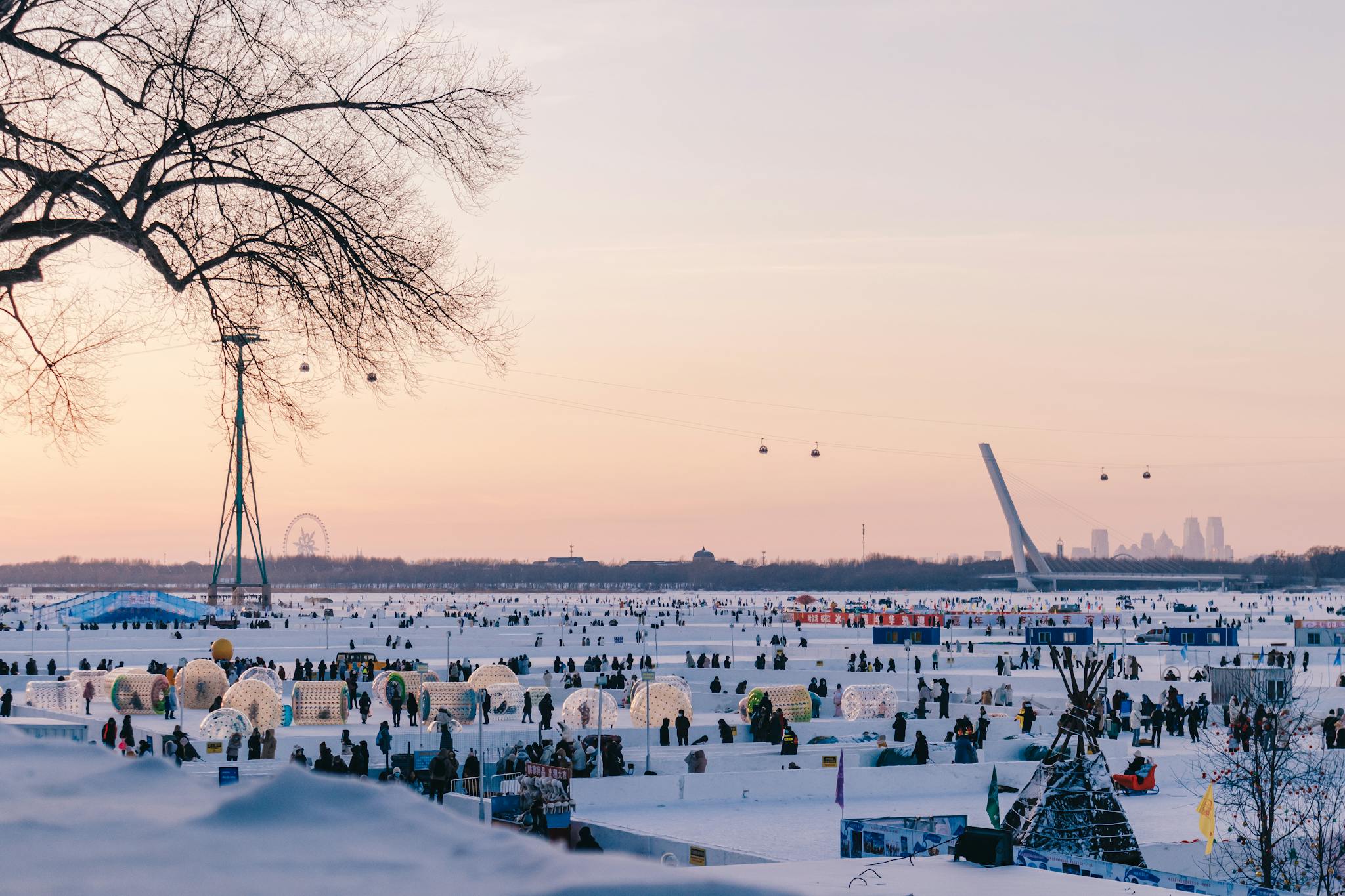 Vibrant winter festival scene with snow structures and crowd at sunset.